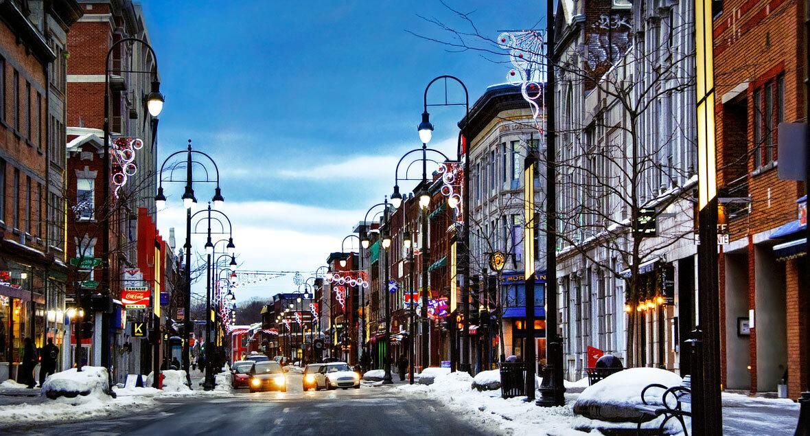 Downtown Trois-Rivières street in winter at dusk, decorated lampposts, brick storefronts and cars with their headlights on