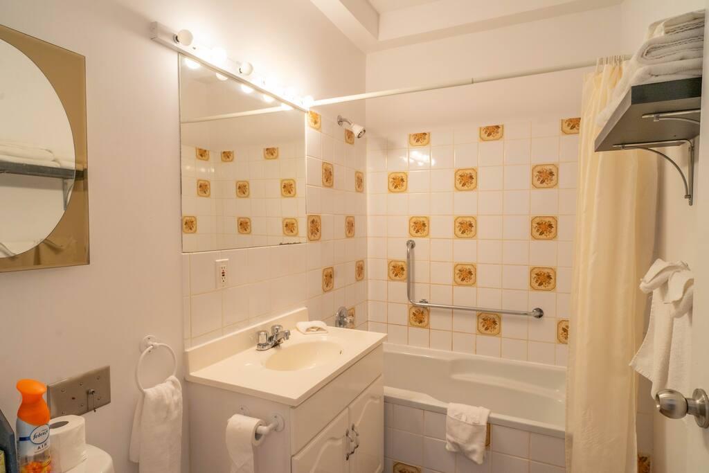 Bathroom with a bathtub-shower with cream floral tile and a grab bar, a round mirror above the sink