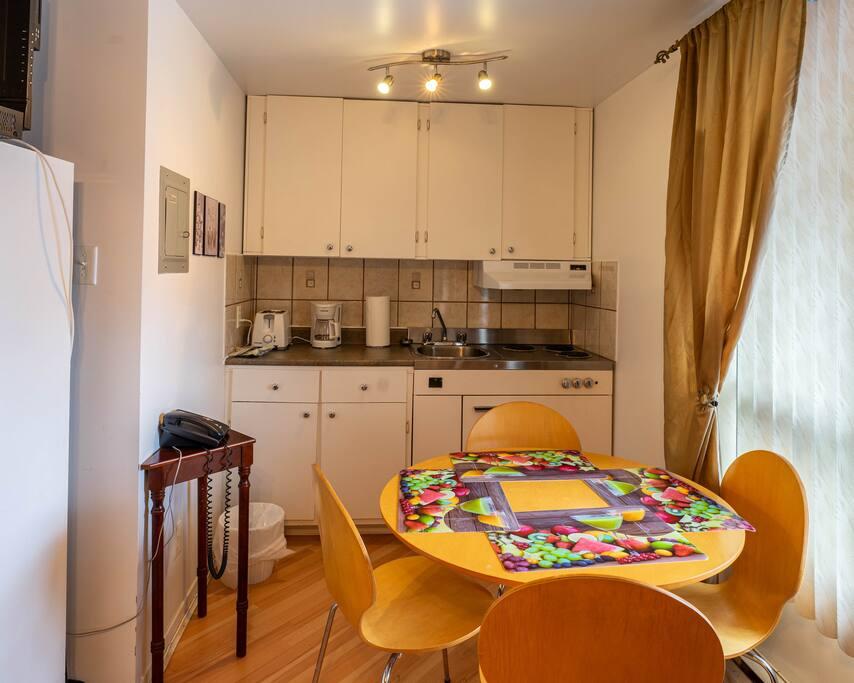 White kitchenette with a round table and four chairs, an electric stovetop and a coffee maker