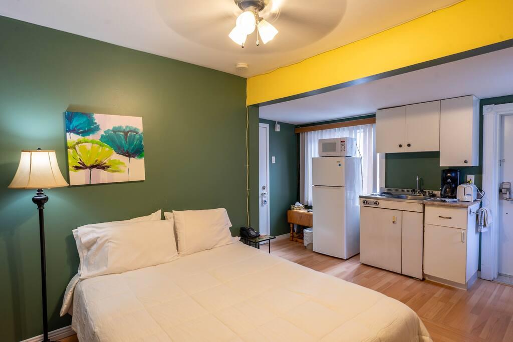 Room with a forest-green accent wall, colourful floral art and a white kitchenette in the background