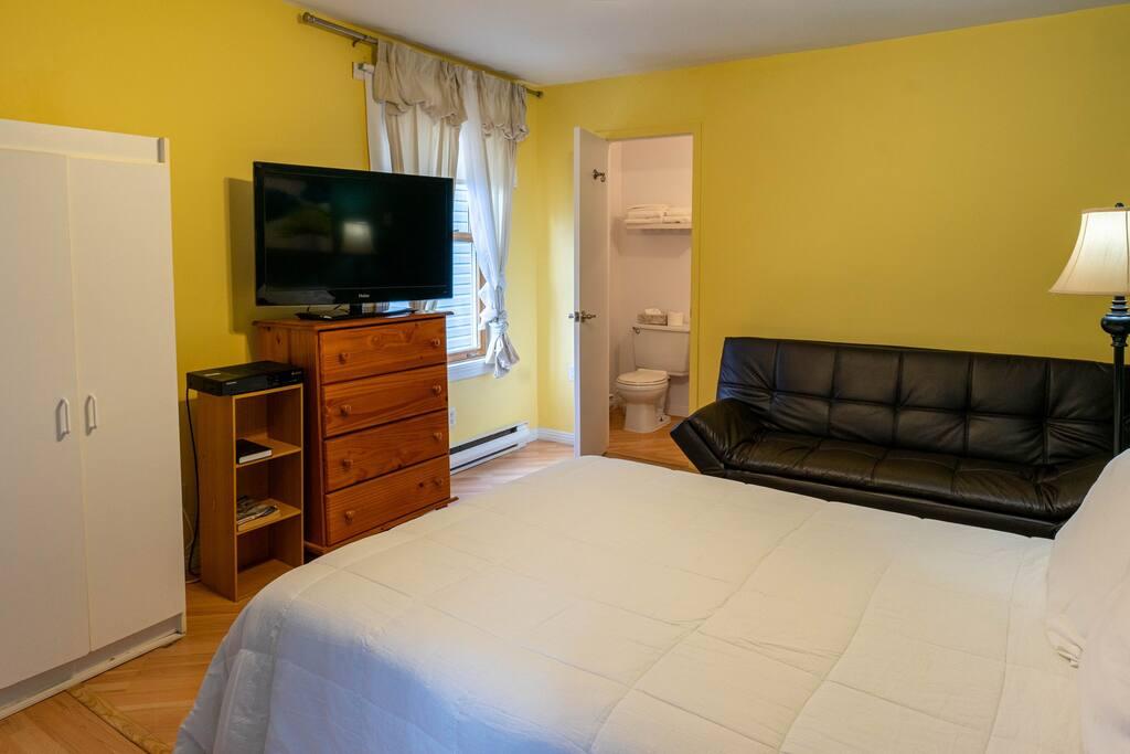 Yellow room with a white bed, a black leather futon and an ensuite bathroom visible through the open door