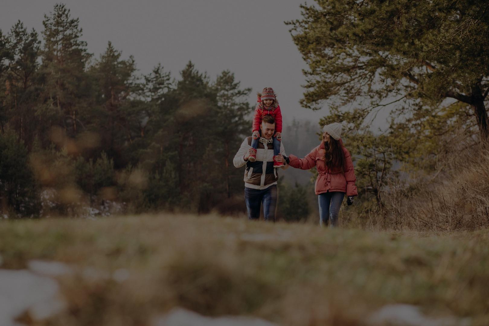 Famille marchant en forêt à l'automne, père portant un enfant sur les épaules et mère à ses côtés
