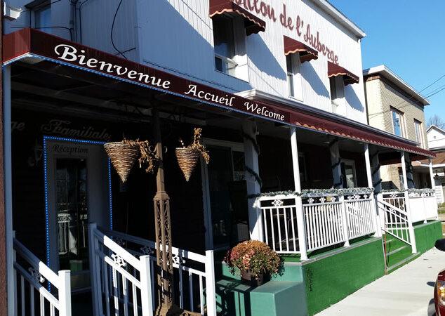 Entrée et réception de l'Auberge La Veranda, porche blanc orné de paniers suspendus sous l'enseigne « Bienvenue Accueil Welcome »