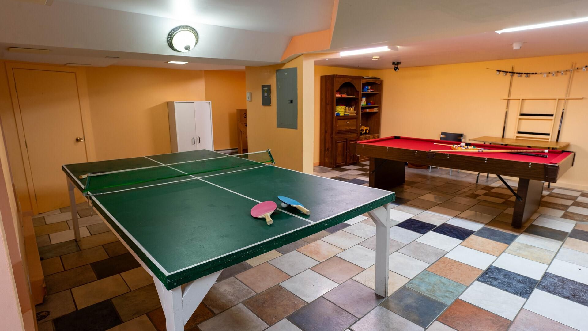 Salle de jeux au sous-sol de l'auberge avec table de ping-pong, table de billard et rangements en bois
