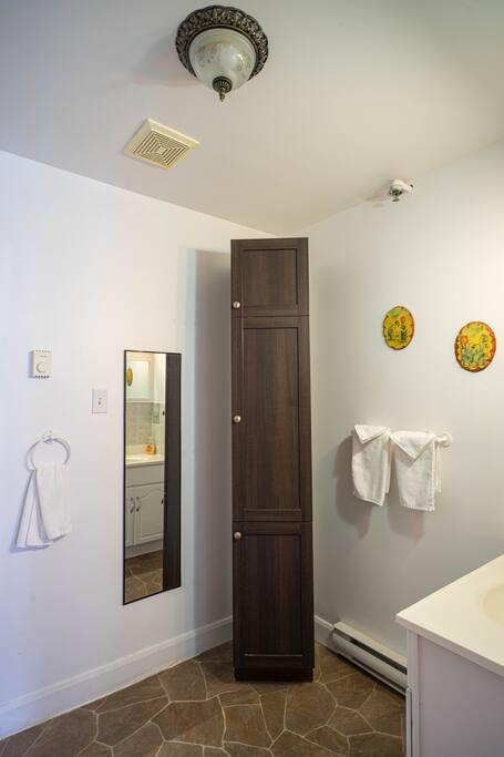 Salle de bain avec armoire de rangement en bois foncé, miroir mural et petite vanité blanche