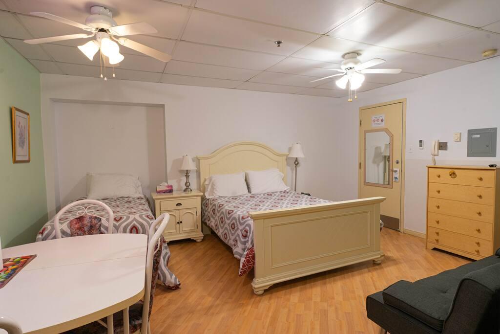 Chambre avec deux fauteuils en cuir bordeaux, commode avec téléviseur et climatiseur mural, mur d'accent jaune