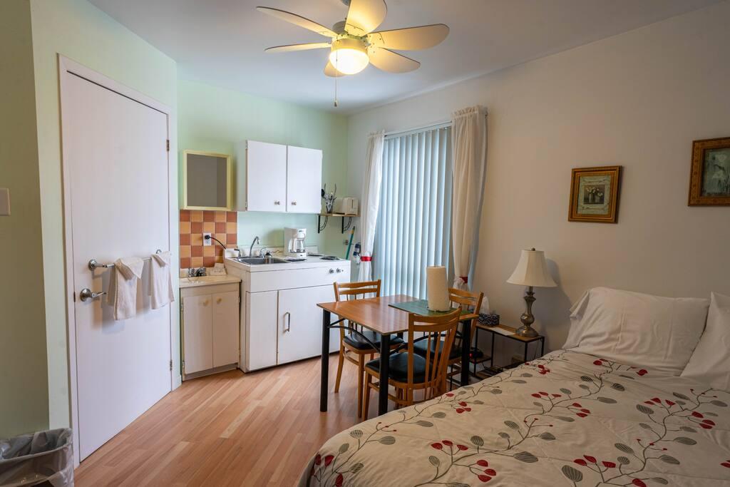 Chambre vert sauge avec cuisinette, table à manger pour quatre et lit à couvre-lit floral crème et rouge