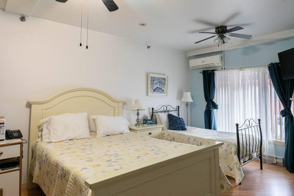 Chambre avec deux lits à couvre-lits floraux gris et jaune, climatiseur mural et rideaux à double épaisseur