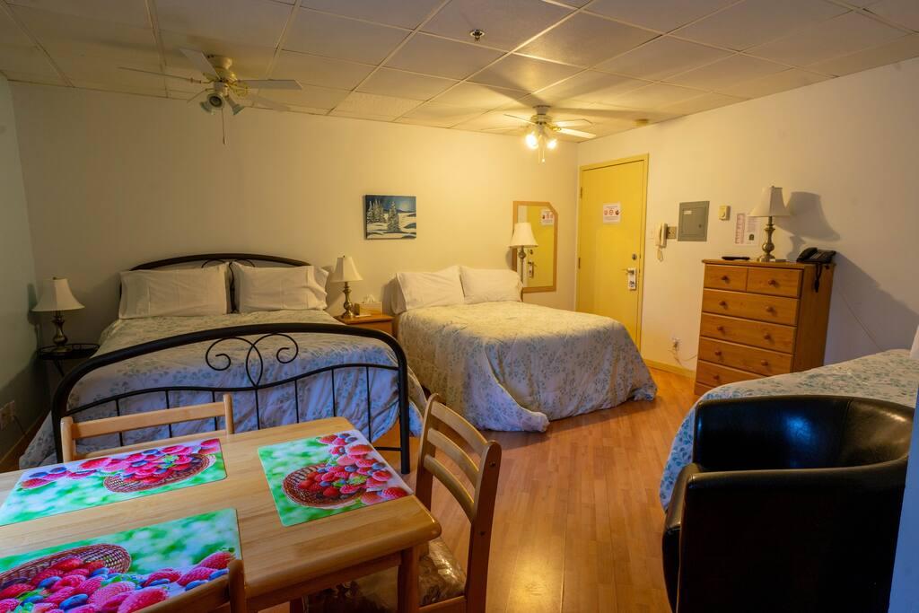 Chambre avec deux lits à couvre-lits floraux bleu pâle, commode-miroir en bois et table à manger au premier plan