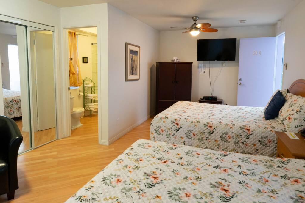 Chambre numéro 304 avec deux lits à couvre-lits floraux, armoire en bois foncé et salle de bain attenante entrevue